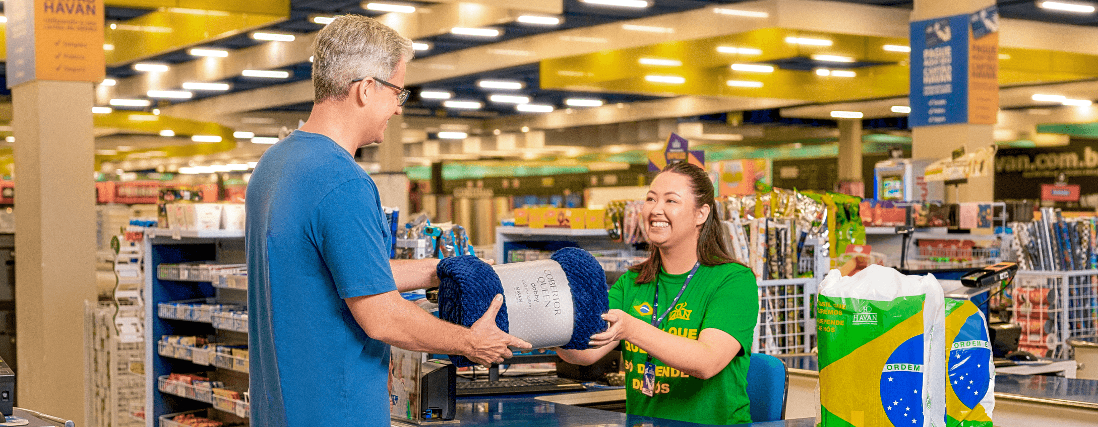 Um cliente no caixa da loja Havan enquanto a colaboradora sorrindo entrega os produtos pra ele